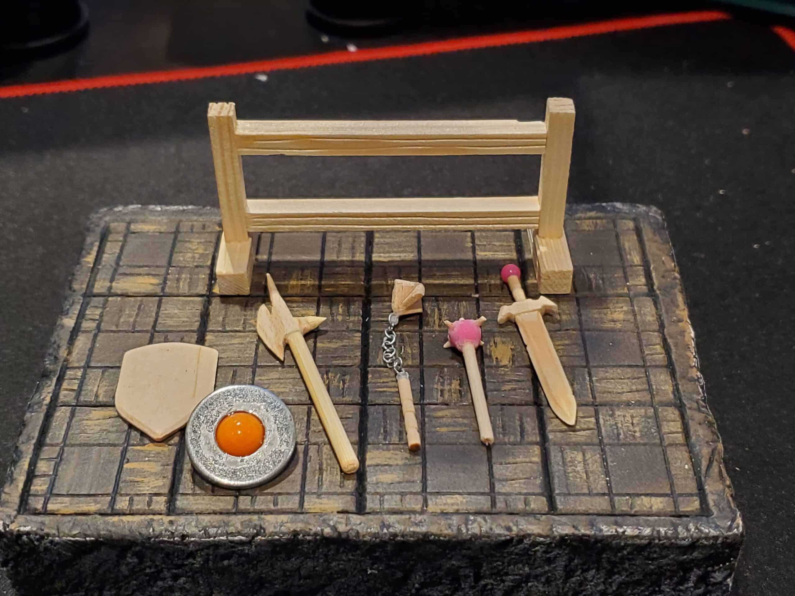 The weapon rack disassembled. Two shields, sword, mace, flail, and a halberd sit in front of the assembled rack ready to be painted.